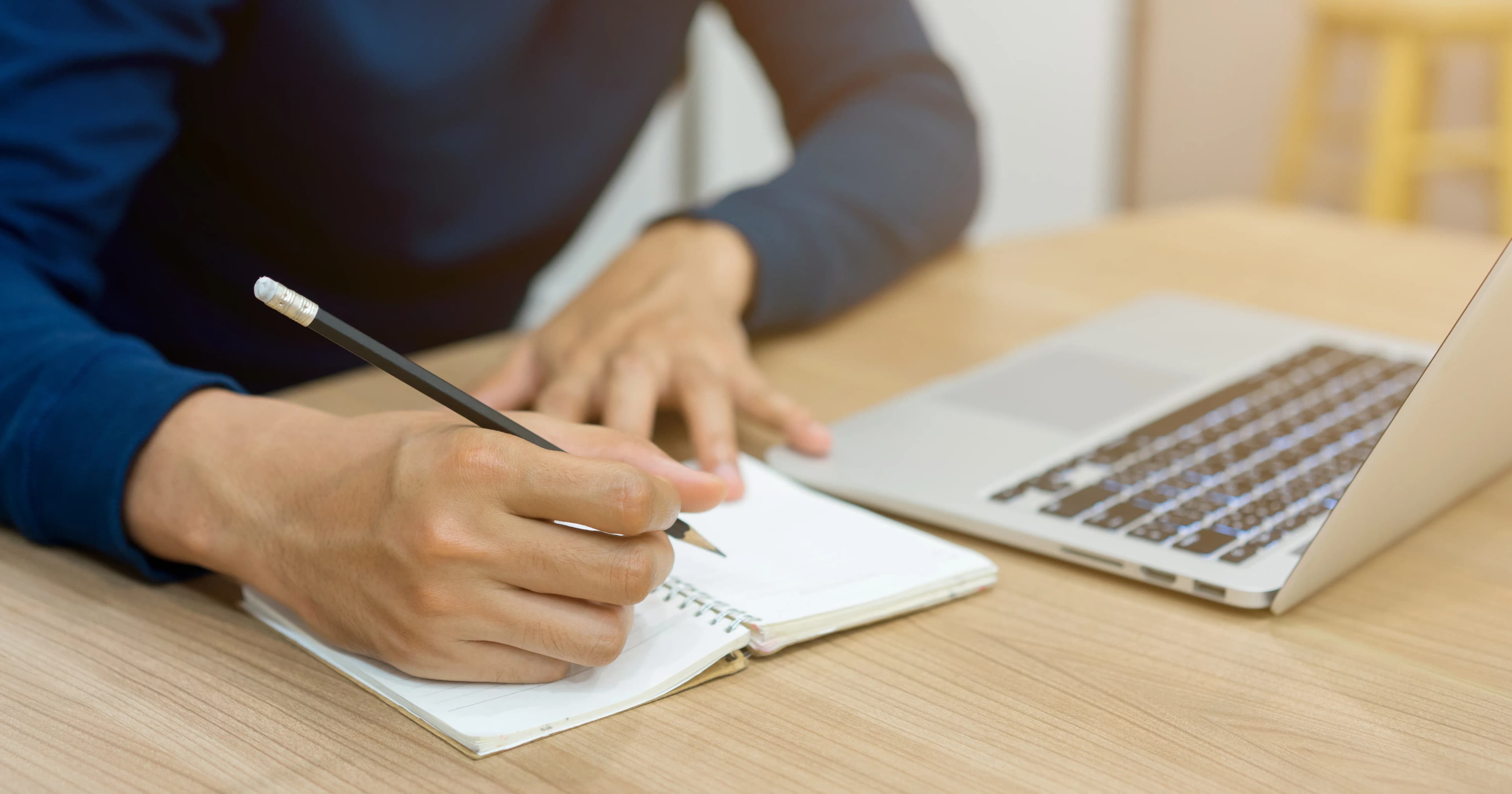 A person writing a content plan in a notebook next to a laptop