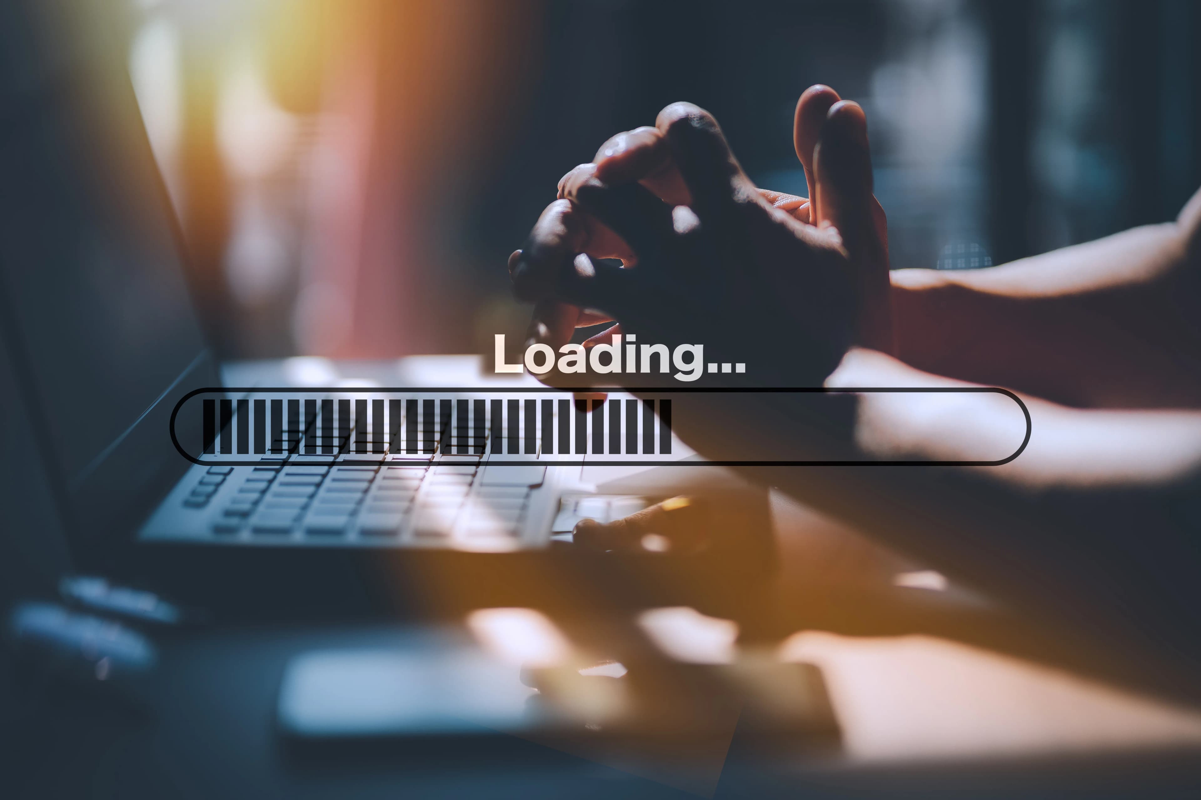 A loading bar on a laptop screen with hands waiting on the keyboard