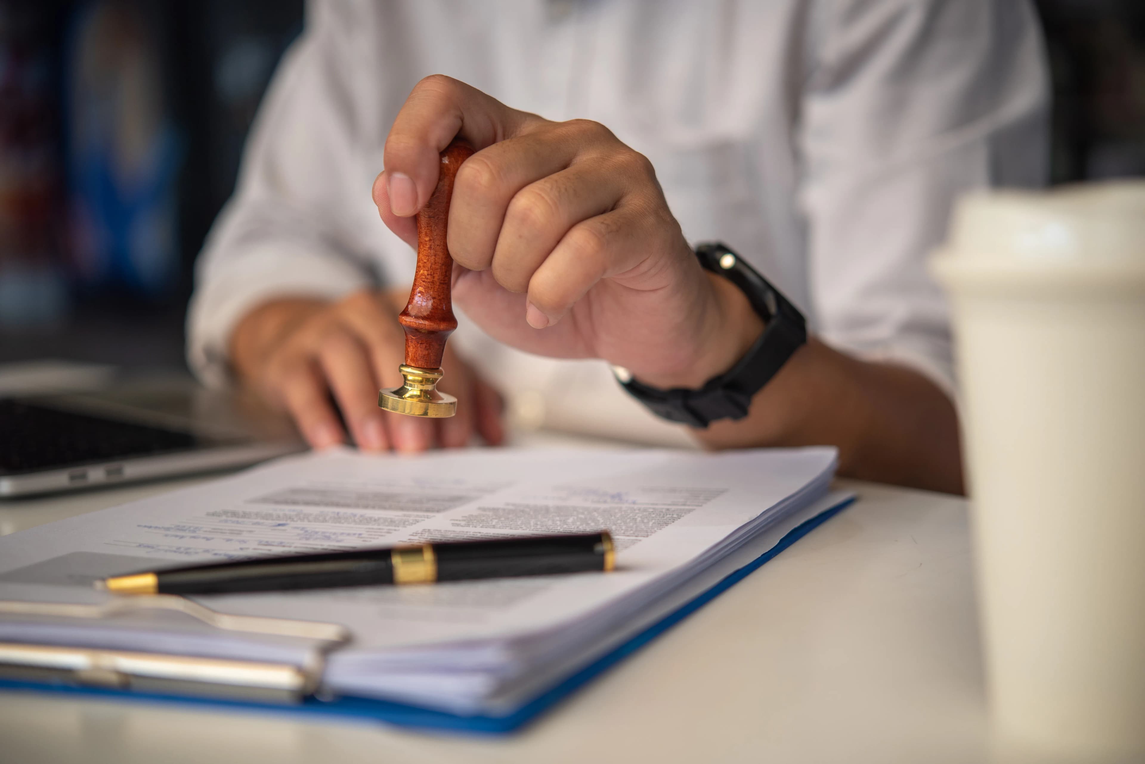 A hand stamping a document on a desk with a fountain pen beside it