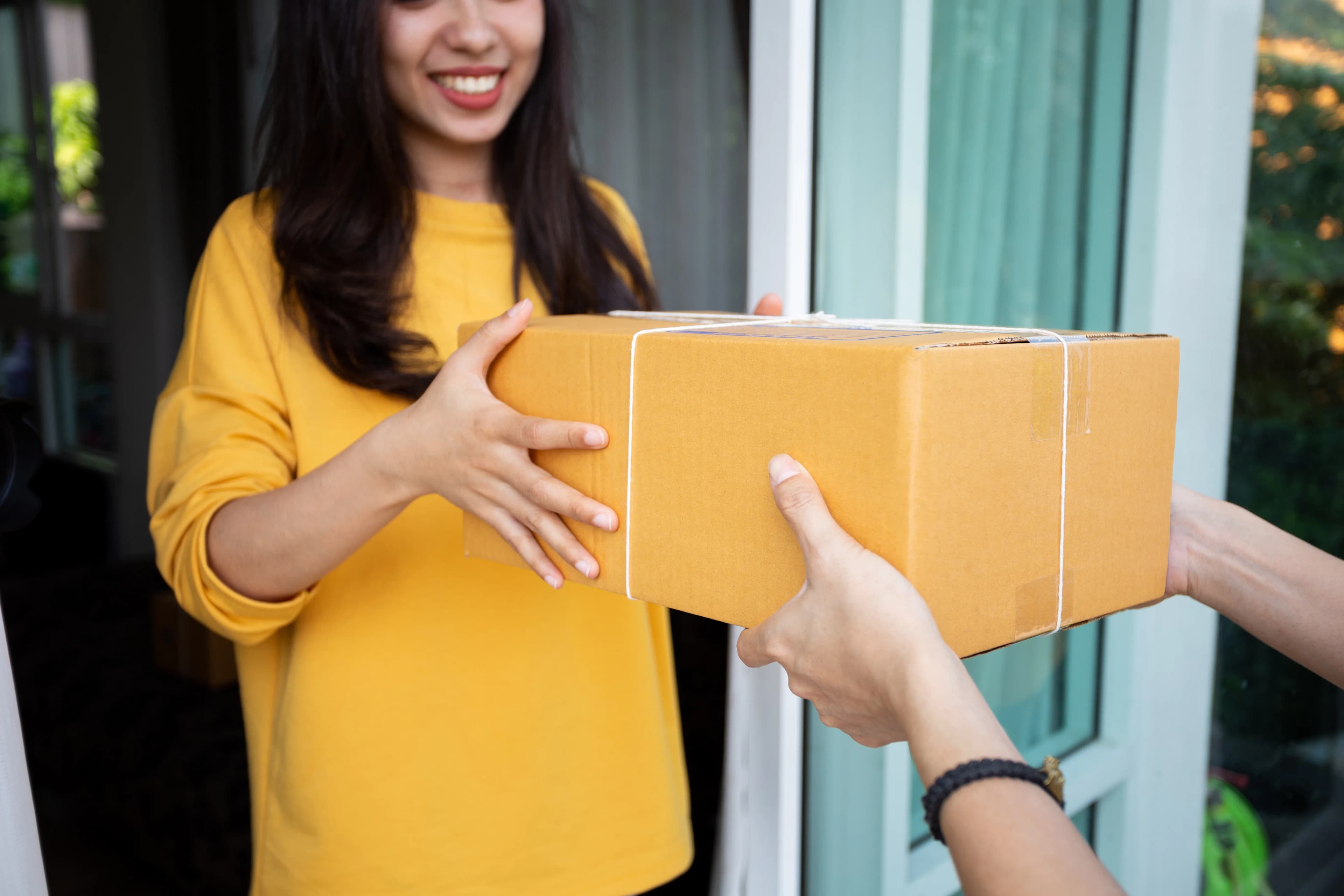 A smiling woman receiving a parcel from a courier at the door