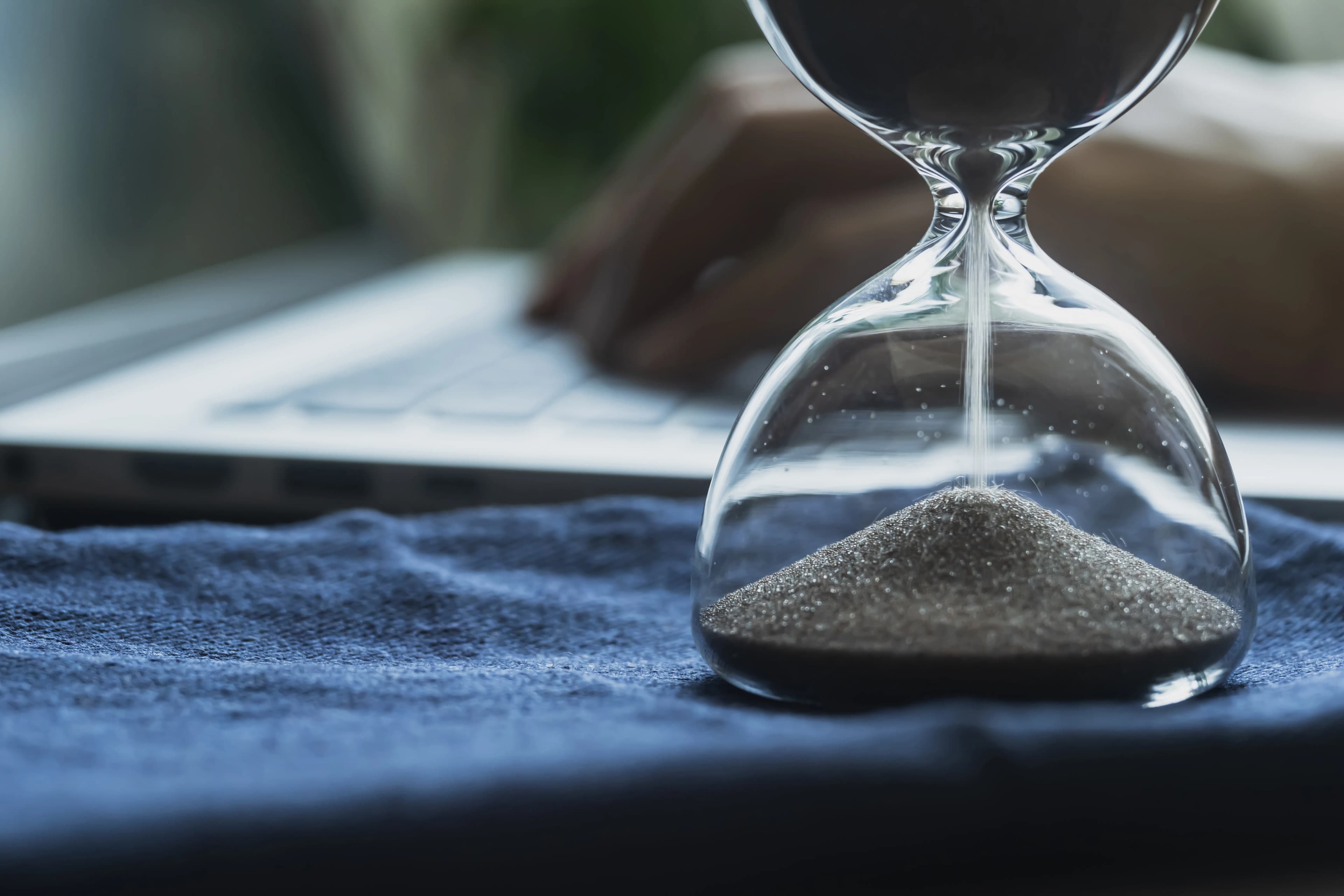 An hourglass running in front of a laptop on a desk