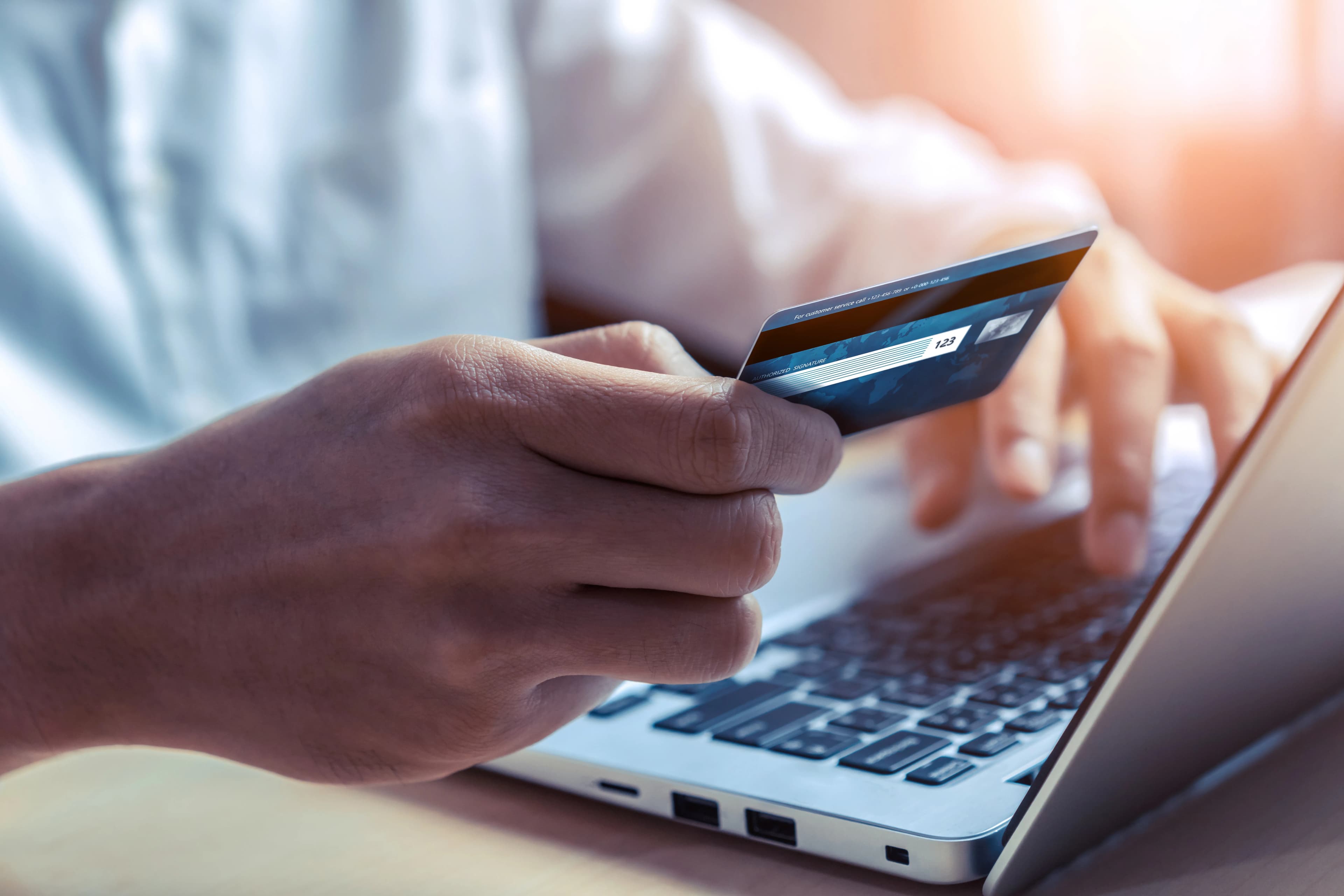 Genç bir adam laptop başında elindeki kredi kartıyla online alışveriş yapıyor