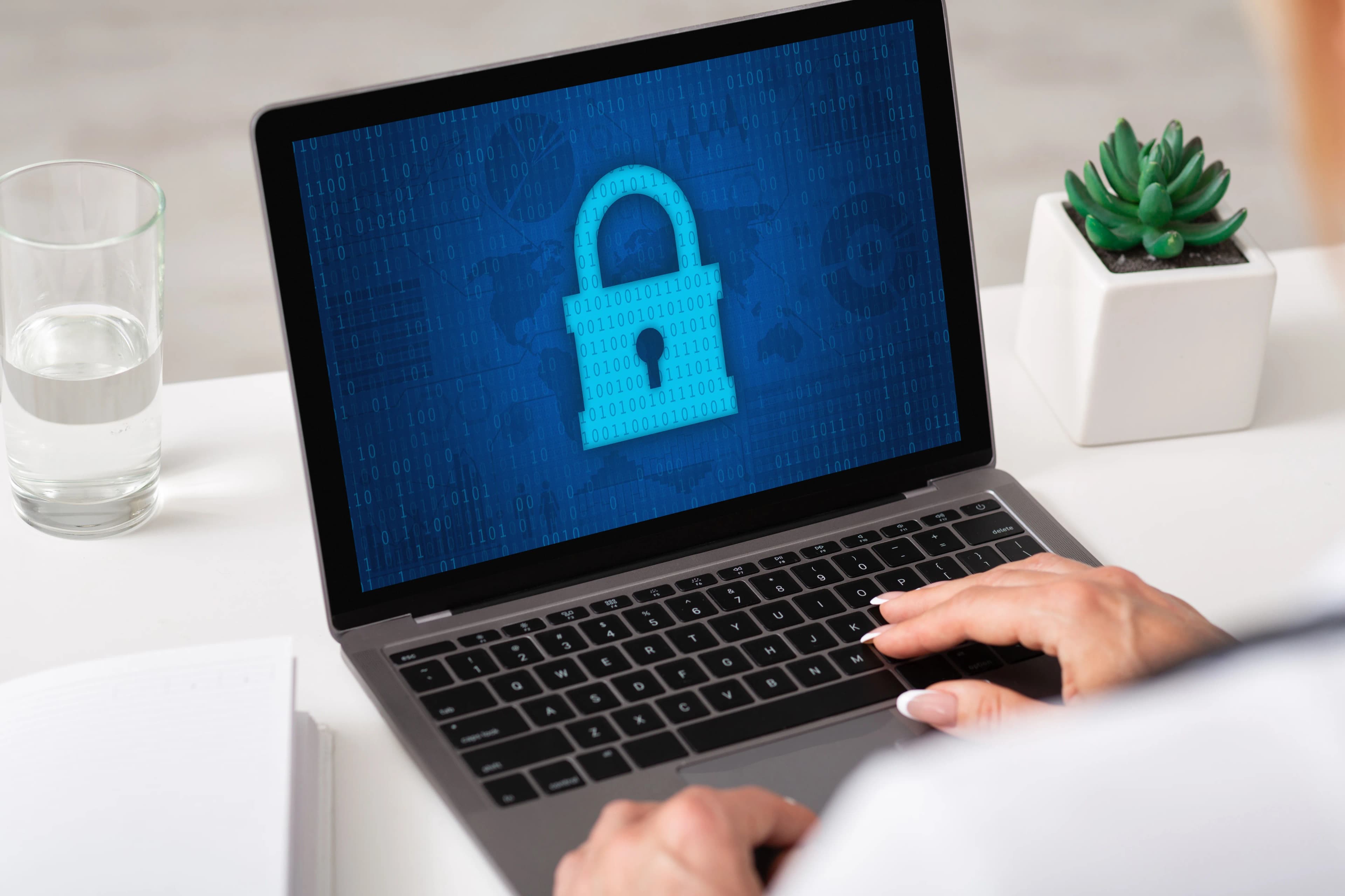 A woman's hand typing on a laptop with a padlock icon on the screen