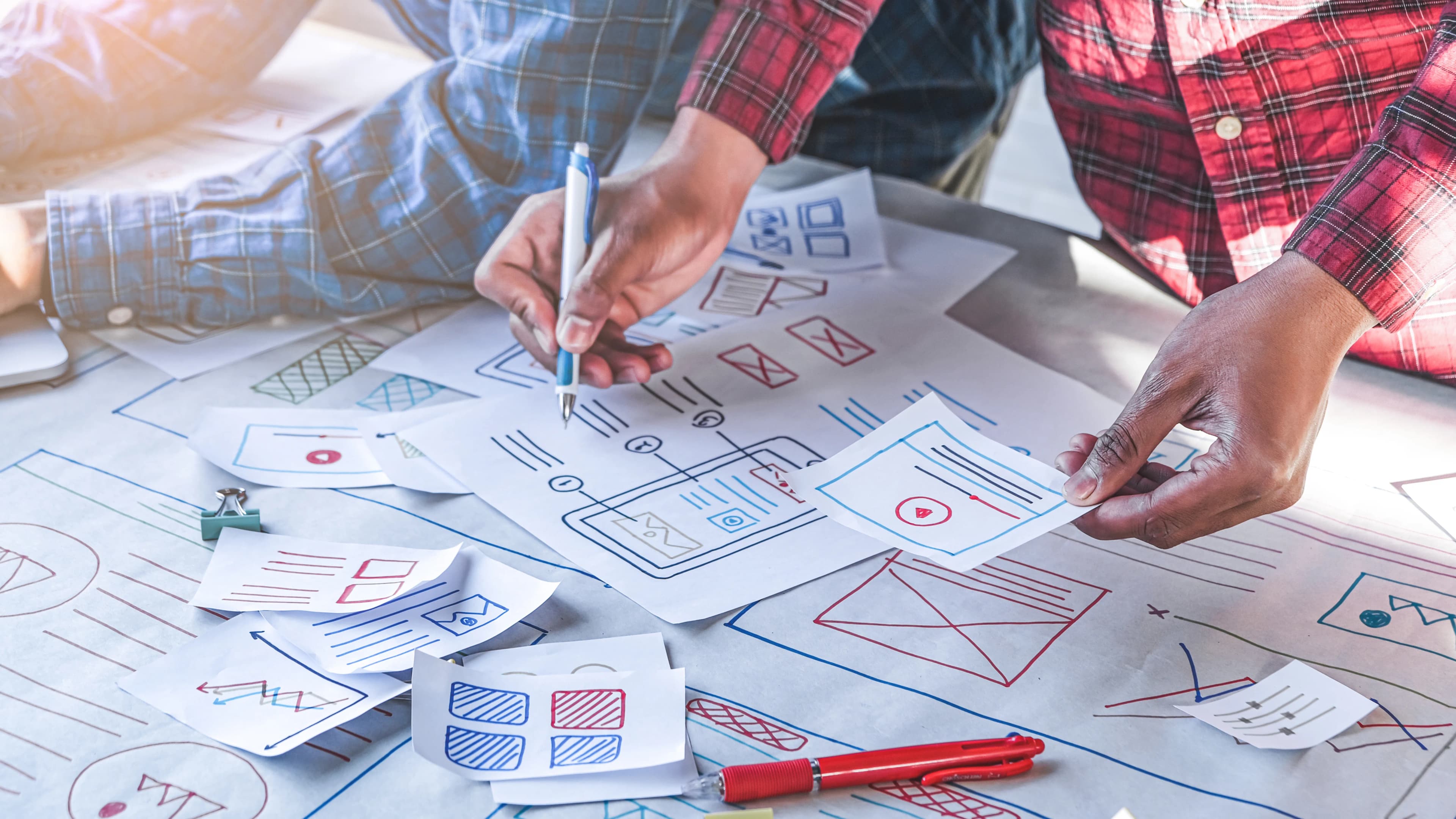 Two UX designers working together over page sketches on a desk