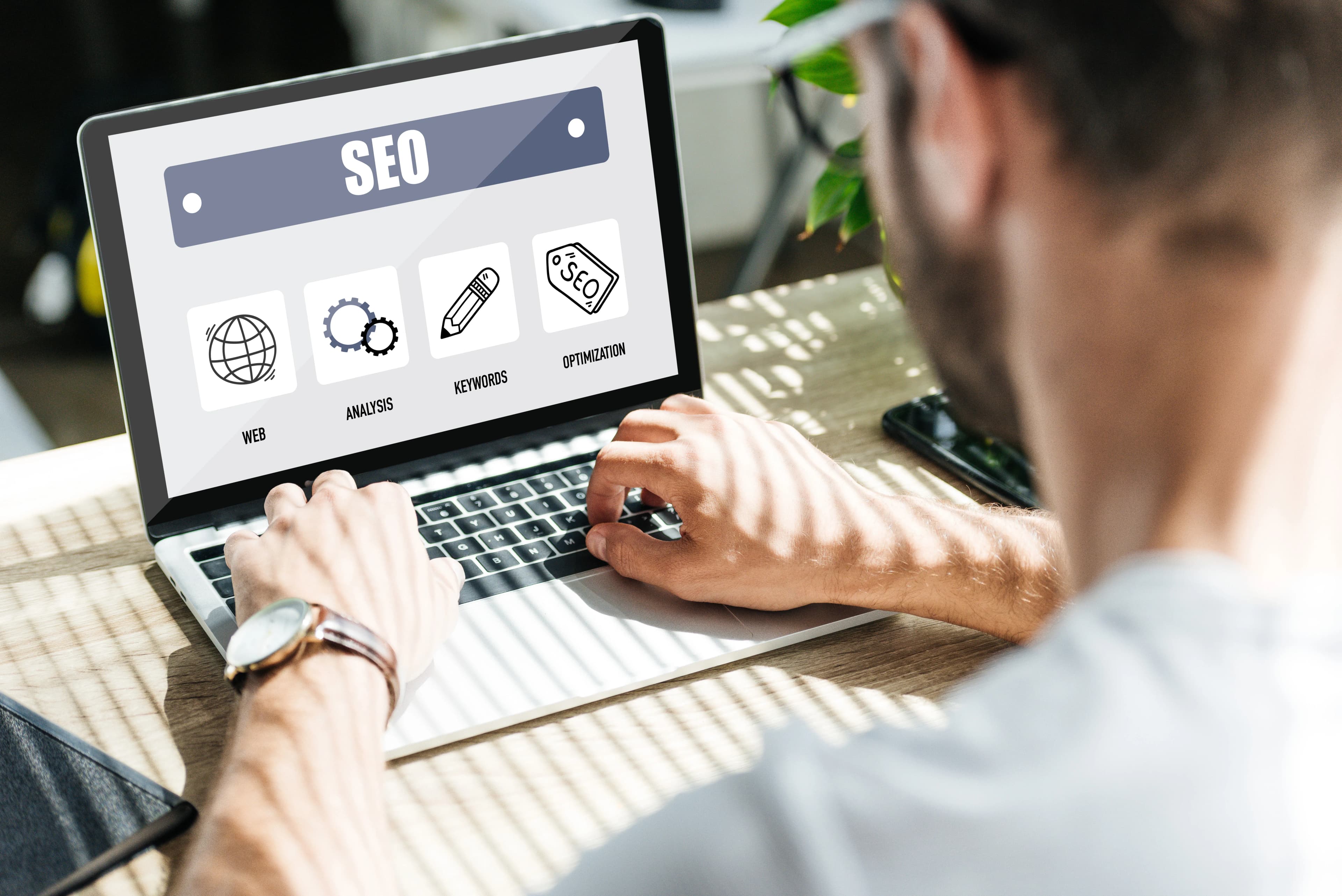 Rear view of a person working at a laptop showing SEO icons on screen