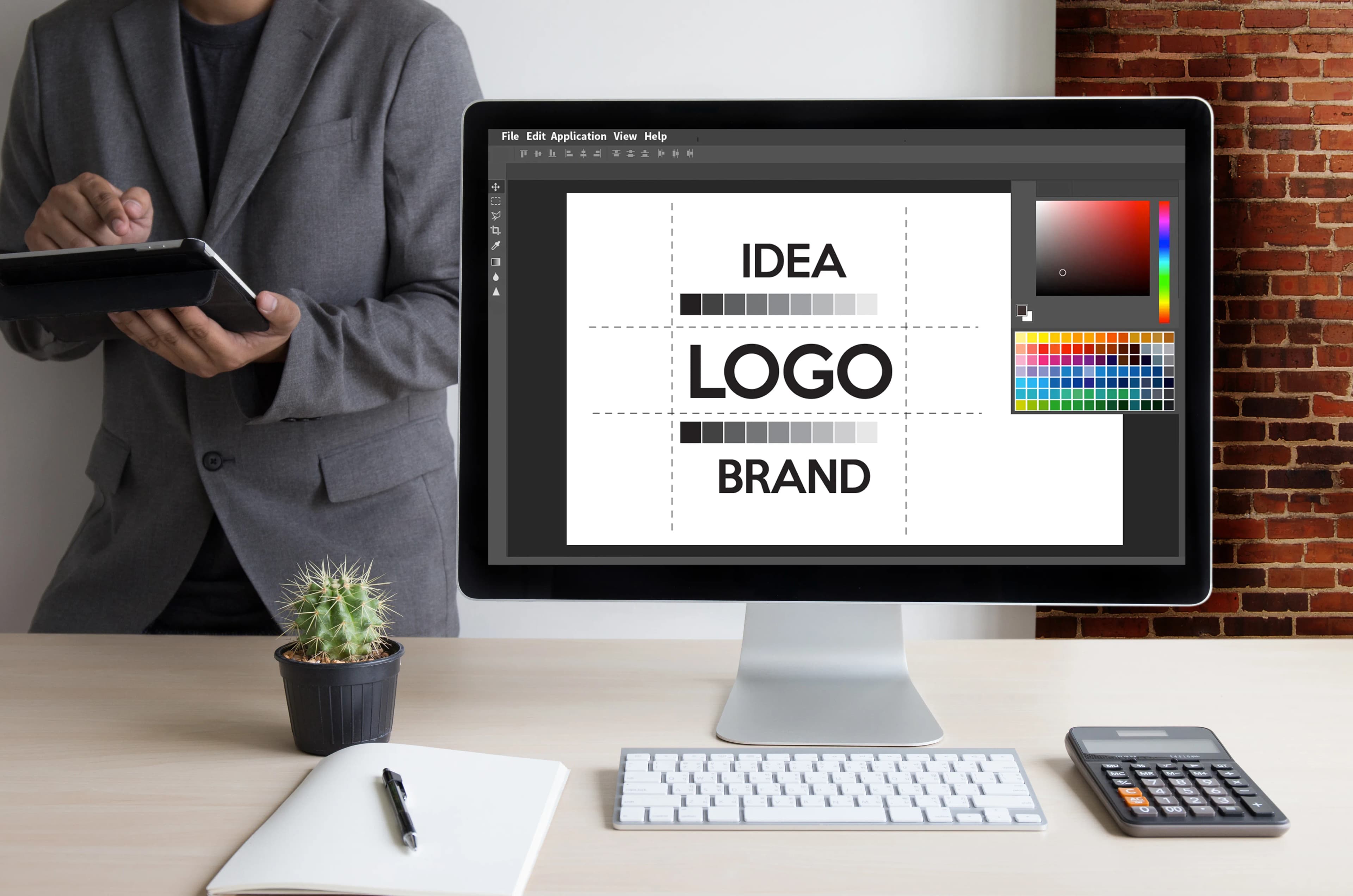 Tasarımcının masasındaki monitörde idea, logo, brand yazılı marka kimliği çalışması