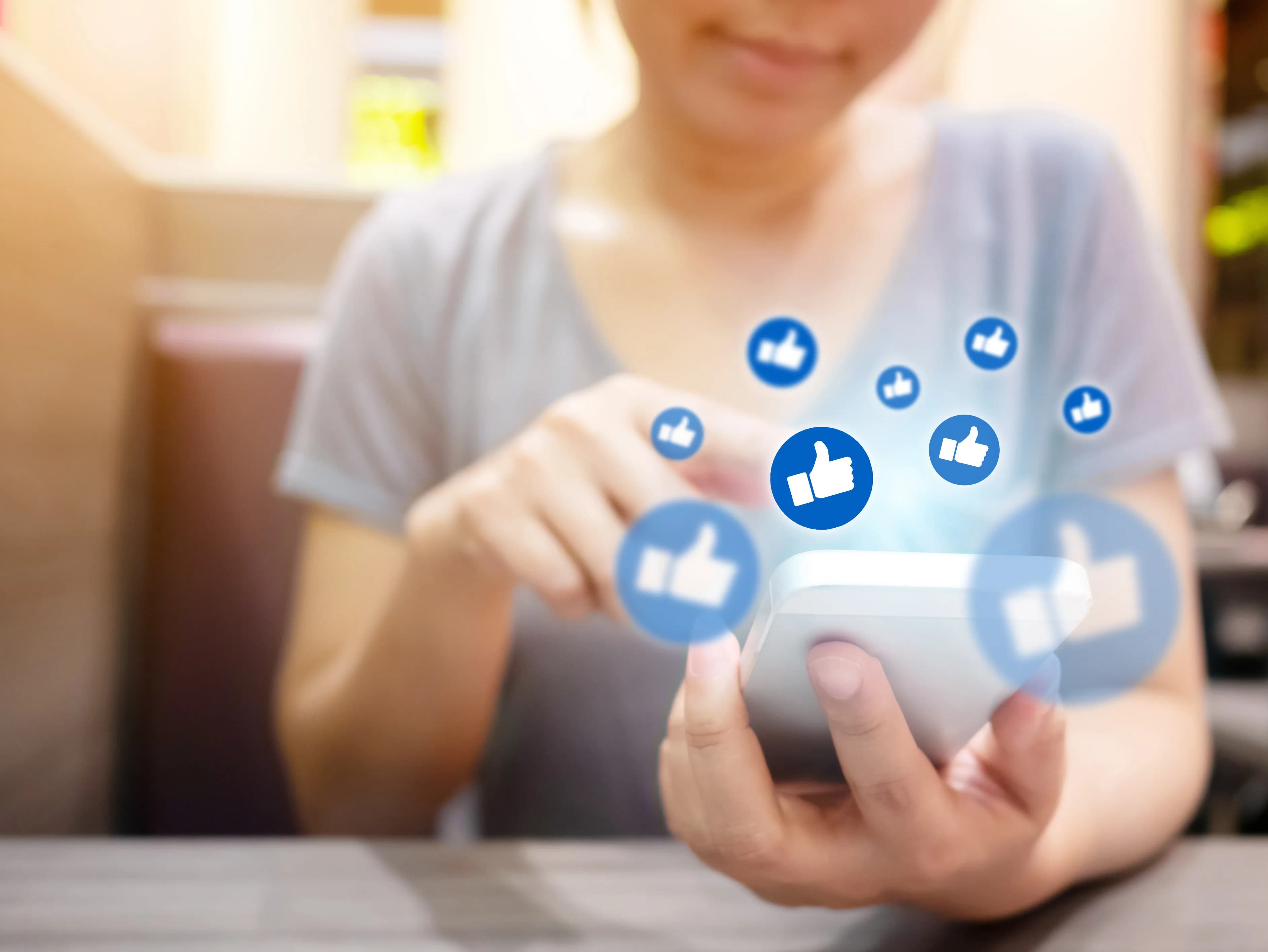 Like and comment icons above a hand-held smartphone