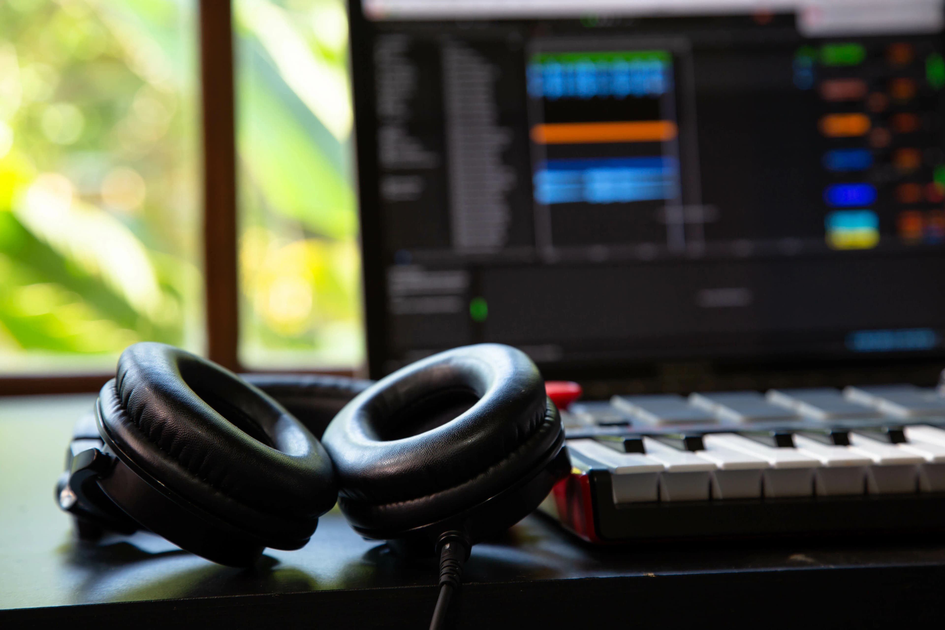 Ev stüdyosunda kulaklık, MIDI klavye ve ekranda müzik yazılımı