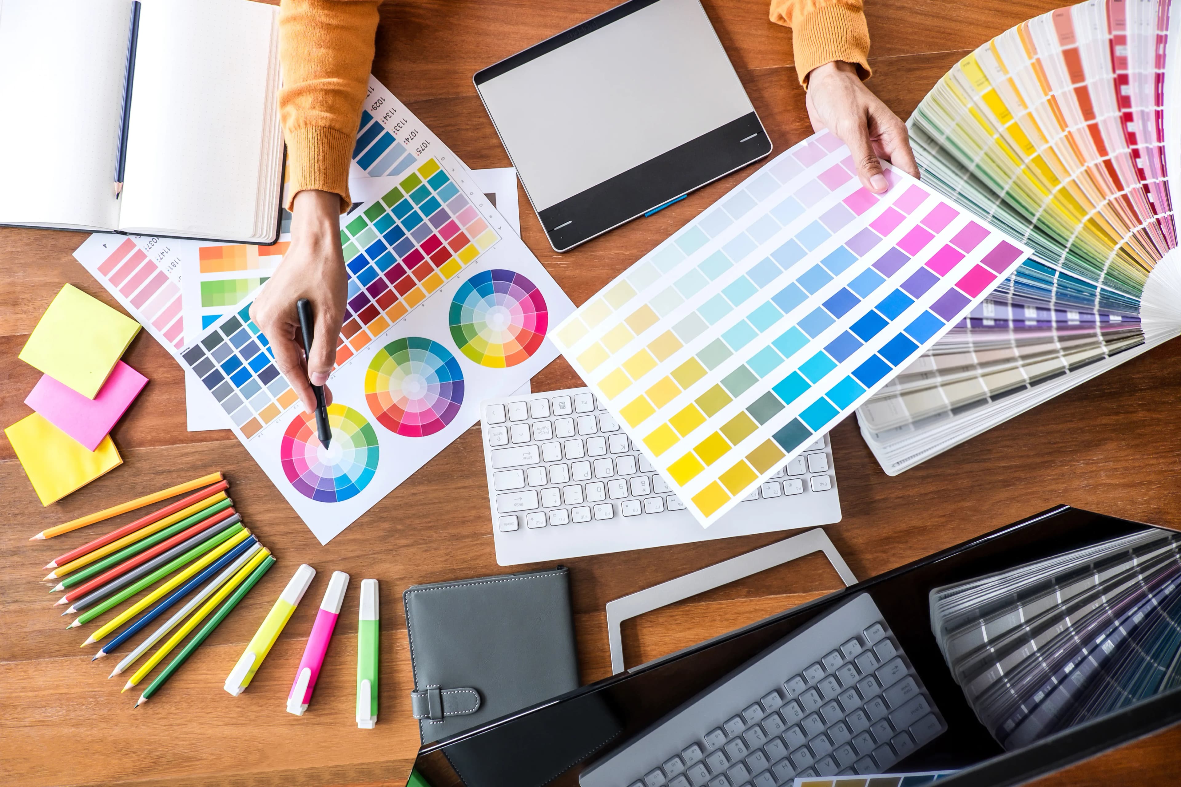 Grafik tasarımcı masasında renk kartelaları, çizim tableti ve laptop, üstten görünüm