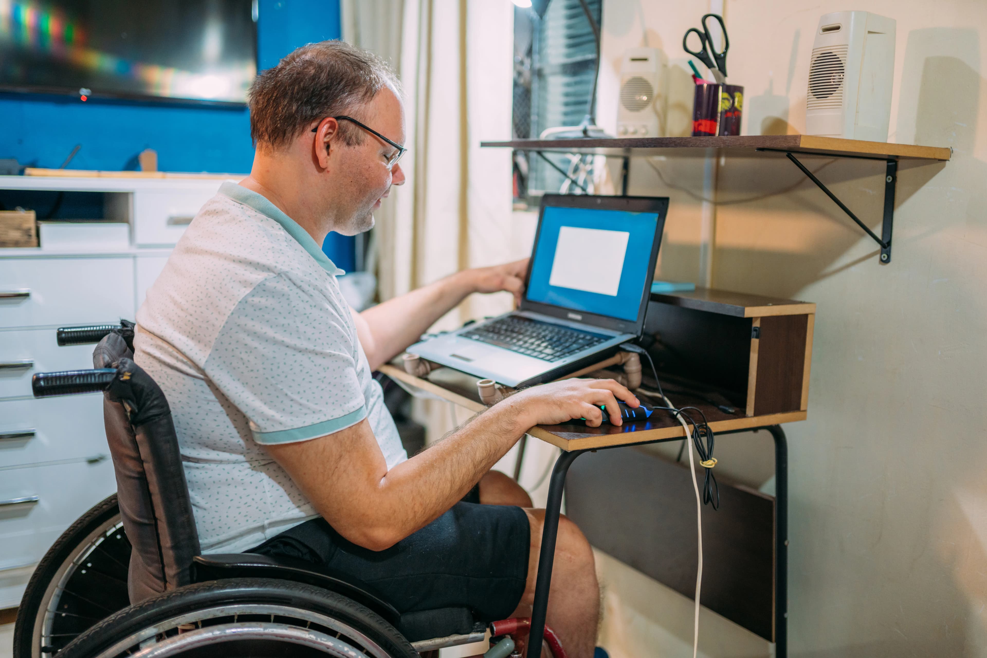 Tekerlekli sandalyedeki bir adam evinde masada laptop kullanıyor