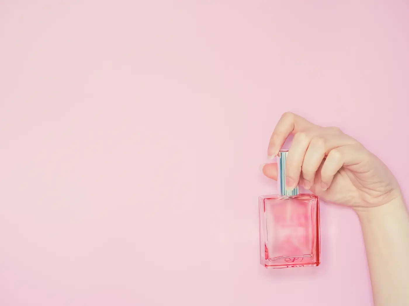 Parfüm şişesi tutan el — pastel pembe fon